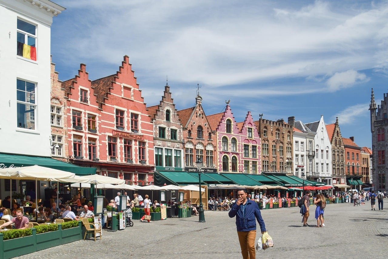 브뤼헤 마르크트 광장, 화려한 색감의 계단식 지붕 건물들과 야외 카페 테라스가 어우러진 활기찬 유럽 광장의 풍경입니다.