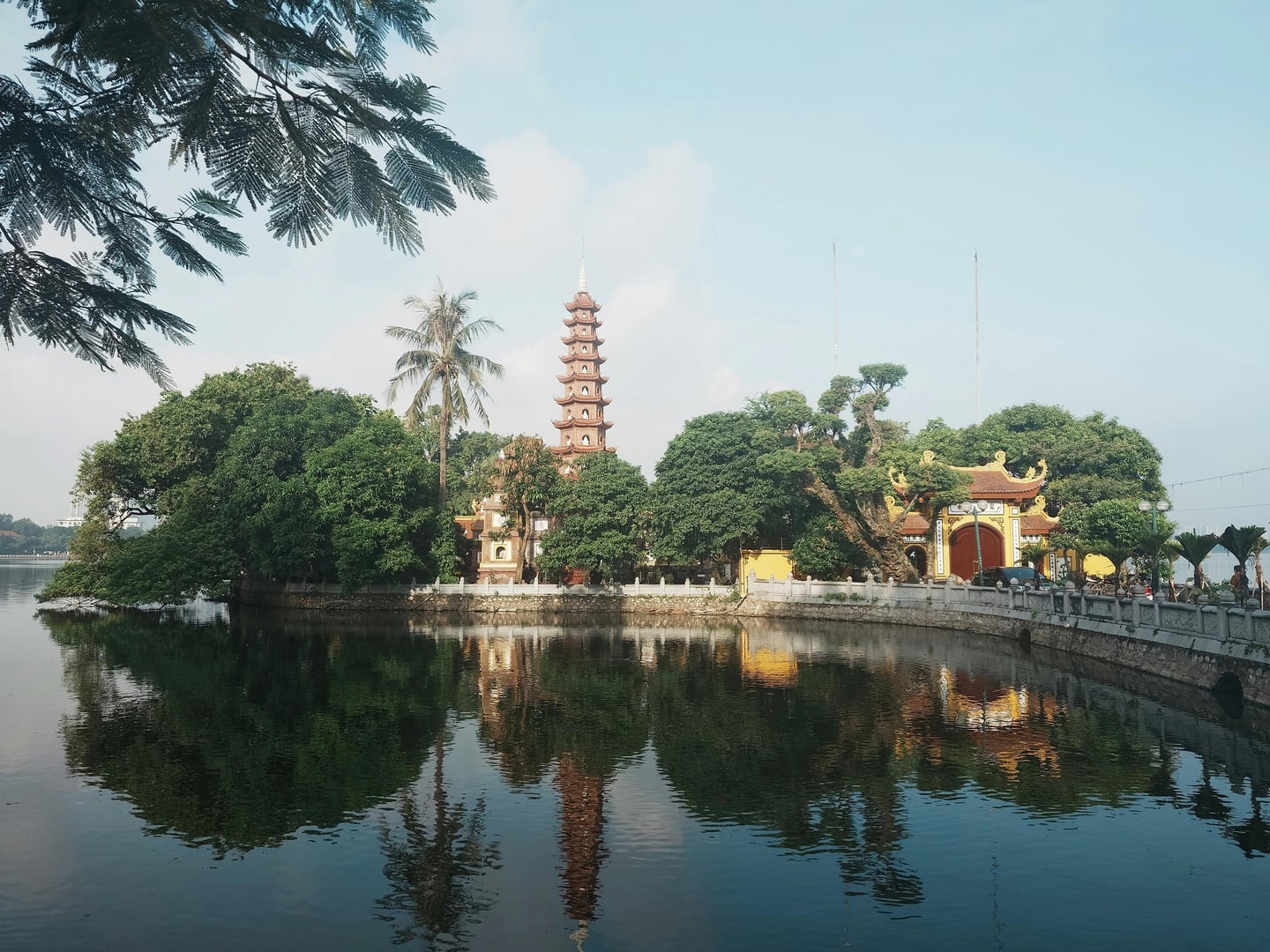 하노이 서호 쩐꾸옥 사원, 잔잔한 호수 위로 붉은색 다층 탑과 울창한 나무들이 거울처럼 반사되는 평화로운 풍경입니다.