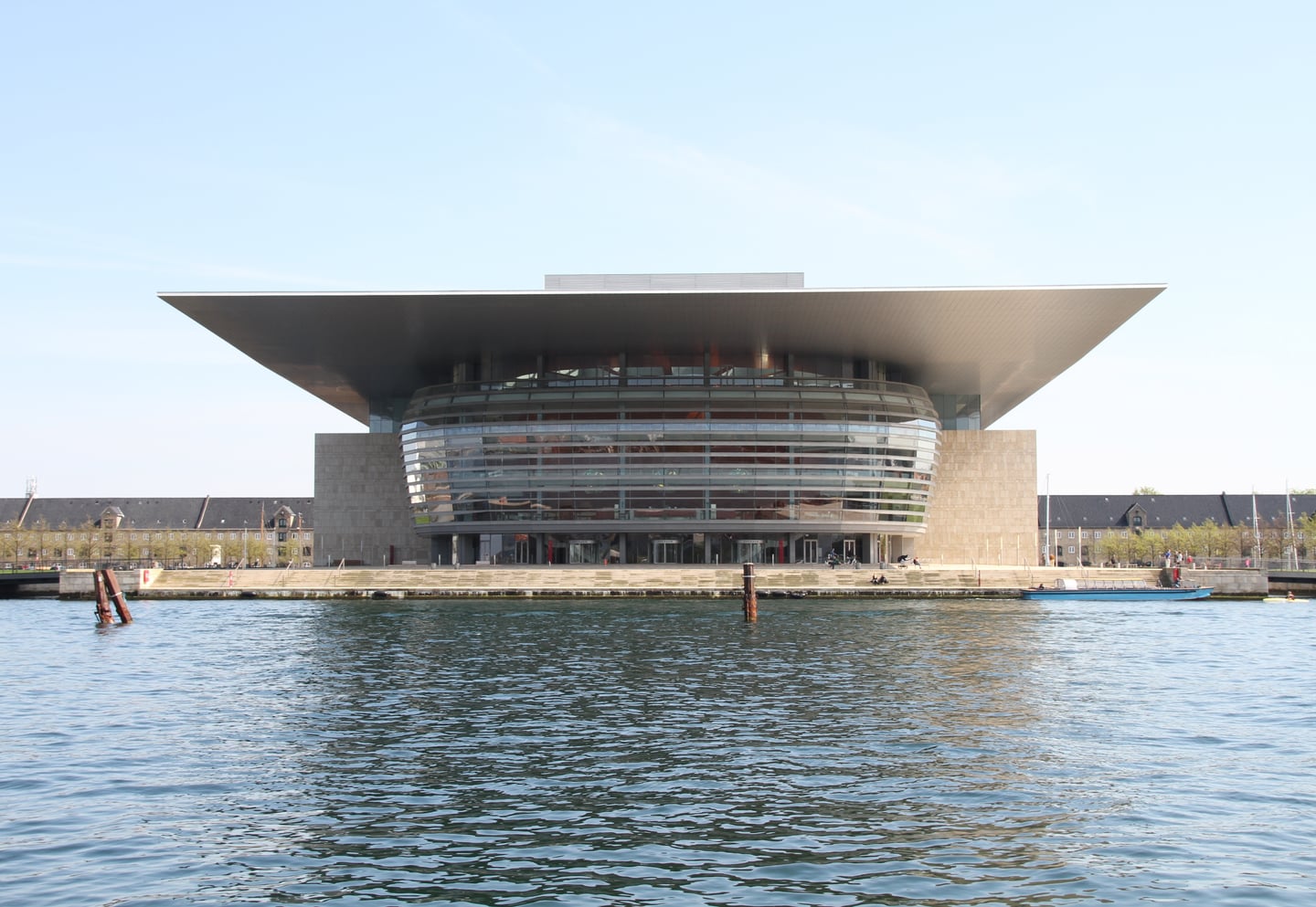 코펜하겐 왕립 오페라 하우스, 푸른 운하 너머로 보이는 웅장하고 현대적인 캔틸레버 지붕과 전면 유리창이 돋보이는 건축물 전경입니다.