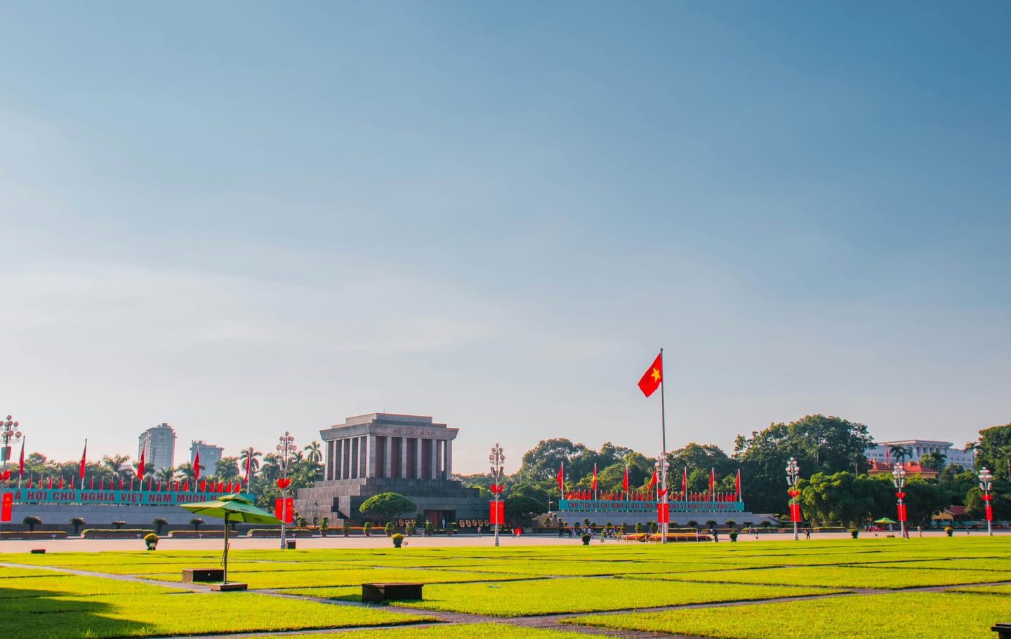 하노이 바딘 광장, 푸른 잔디밭 너머로 보이는 웅장한 호치민 묘소와 맑은 하늘 아래 펄럭이는 베트남 국기.
