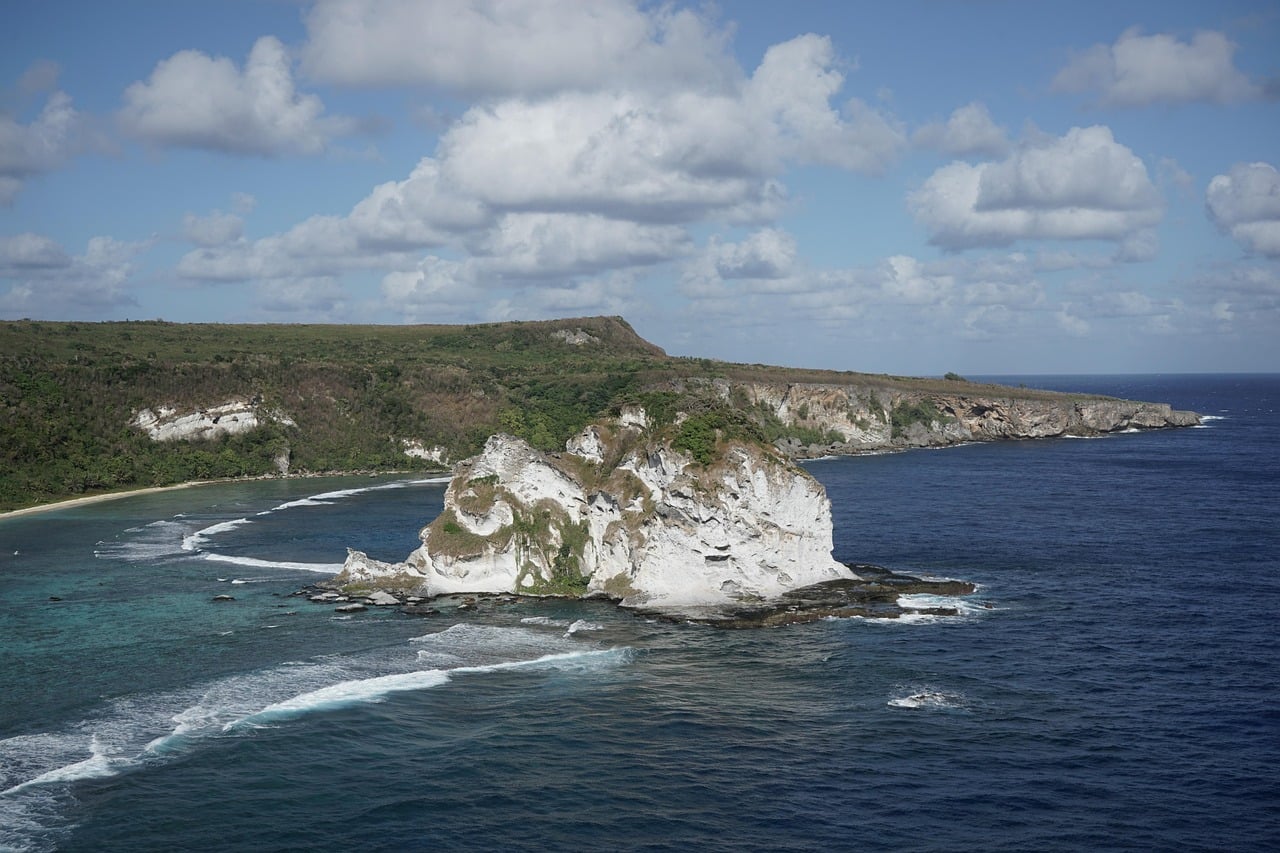 사이판 새섬, 에메랄드빛 바다 위에 우뚝 솟은 하얀 석회암 섬과 굽이치는 파도가 만들어내는 평화로운 해안 절경입니다.