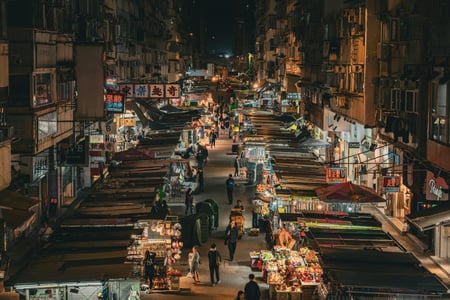 홍콩 몽콕 야시장, 낡은 고층 건물 사이로 화려한 조명이 켜진 노점상들이 길게 늘어선 활기찬 밤거리 풍경입니다.