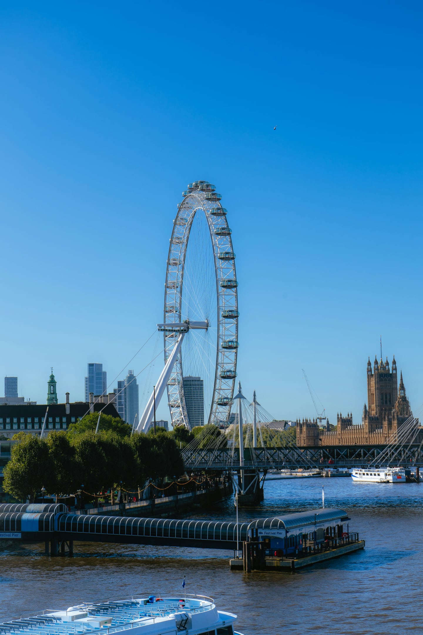 런던 템스강, 푸른 하늘 아래 런던 아이와 웨스트민스터 궁전이 어우러진 평화로운 강변 풍경입니다.