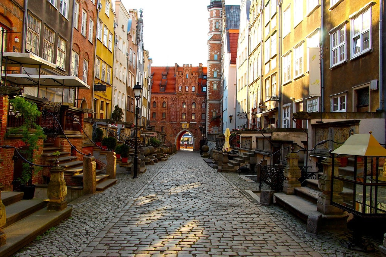 그단스크 마리아츠카 거리, 자갈길을 따라 늘어선 고풍스러운 테라스 건물들과 붉은 벽돌 성문이 어우러진 풍경입니다.