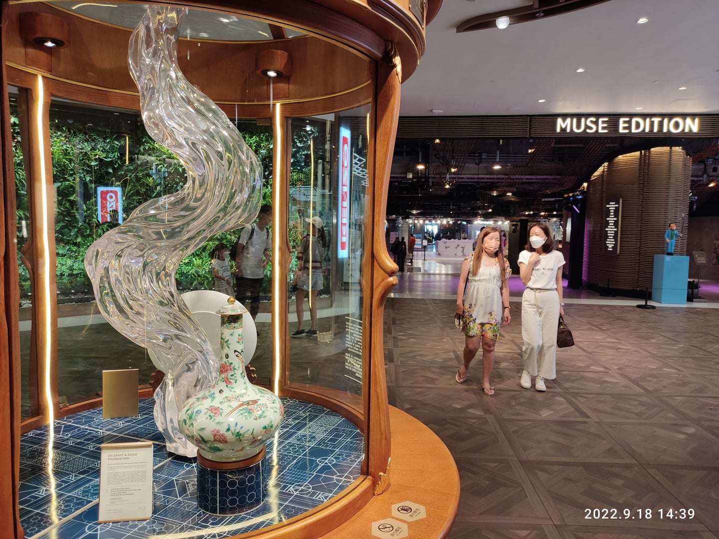 홍콩 침사추이 K11, 화려한 유리 조형물과 도자기가 전시된 쇼케이스 너머로 뮤즈 에디션 매장을 지나는 사람들의 모습입니다.