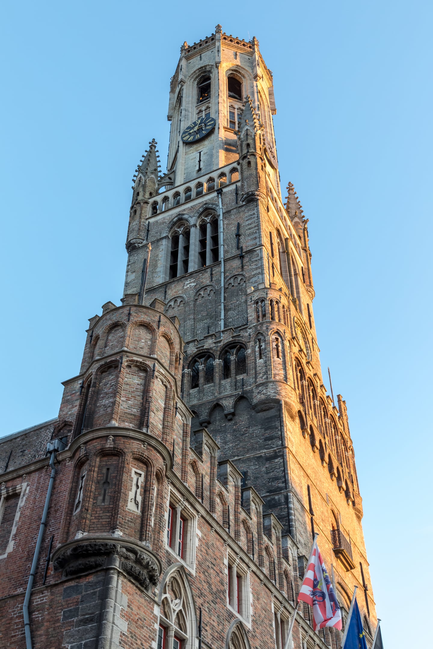 브뤼헤 종루, 황금빛 노을을 받아 따뜻한 색감으로 빛나는 고딕 양식의 거대한 벽돌 시계탑과 맑고 푸른 하늘의 조화.