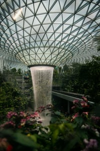 싱가포르 쥬얼 창이, 기하학적인 유리 돔 천장에서 쏟아지는 거대한 실내 폭포와 푸른 정원이 어우러진 웅장한 풍경입니다.