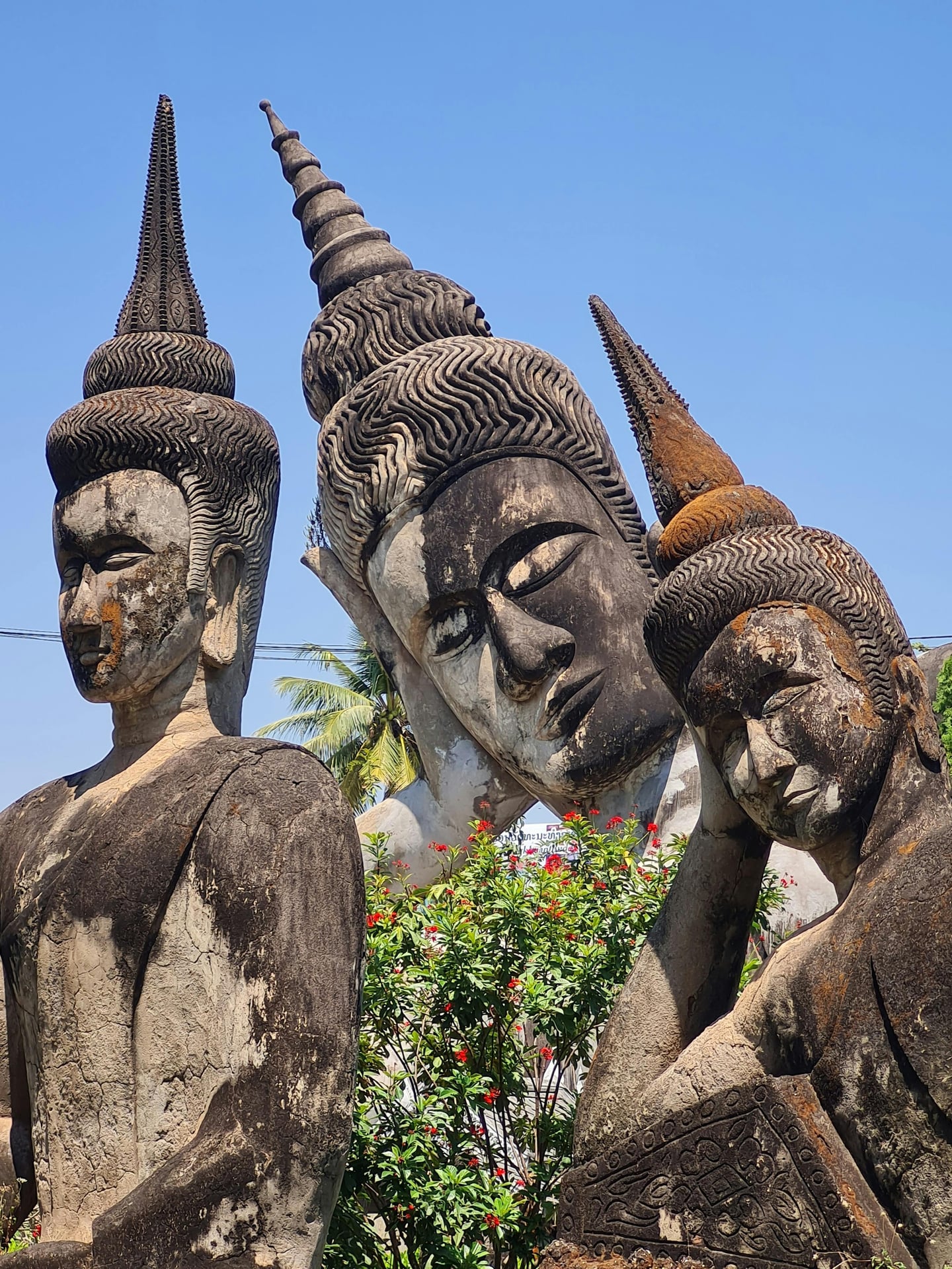 비엔티안 불상 공원, 푸른 하늘 아래 고풍스러운 거대 와불상과 정교하게 조각된 석조 불상들이 조화를 이루는 신비로운 풍경입니다.