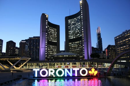 토론토 토론토 신 시청사, 화려한 무지개색 조명이 켜진 토론토 사인과 현대적인 곡선형 시청 건물이 어우러진 아름다운 야경 풍경입니다.