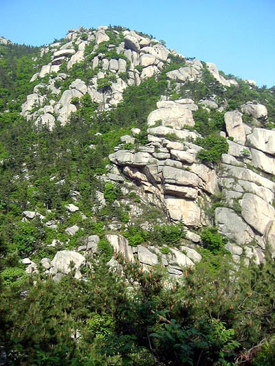 칭다오 노산, 거대한 화강암 기암괴석들이 층층이 쌓여 절경을 이루는 산등성이와 푸른 숲의 조화로운 풍경입니다.