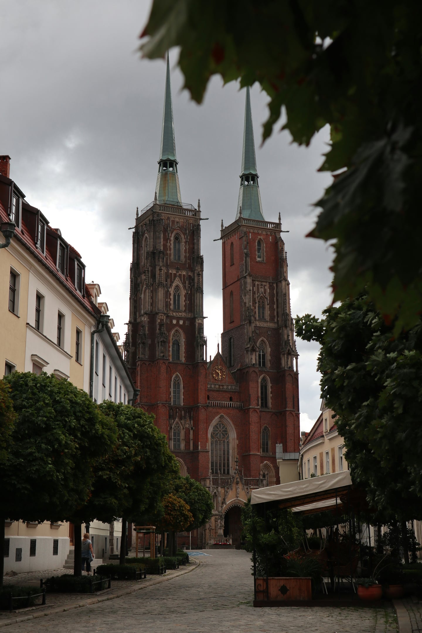 브로츠와프 성 요한 대성당, 고딕 양식의 웅장한 두 첨탑이 흐린 하늘 아래 돌길 끝에서 위엄 있게 솟아 있는 풍경입니다.