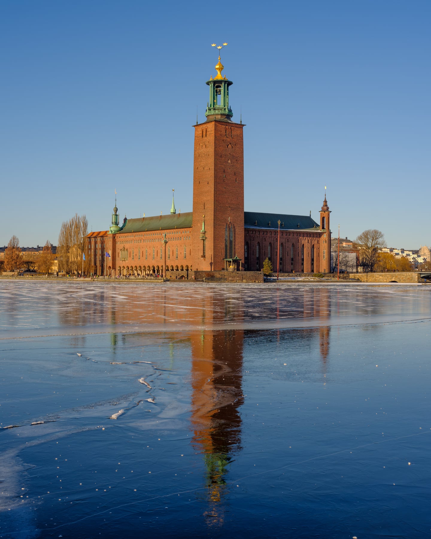 스톡홀름 스톡홀름 시청, 얼어붙은 호수 위로 붉은 벽돌 건물의 웅장한 탑과 푸른 하늘이 아름답게 투영된 겨울 풍경입니다.