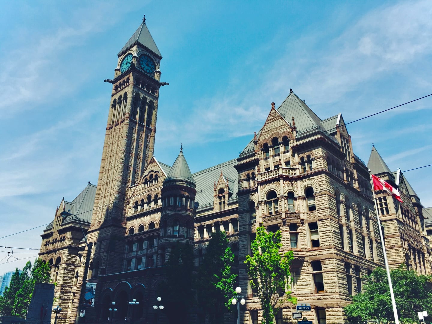 토론토 구 시청사, 푸른 하늘을 배경으로 웅장하게 솟은 고전적인 시계탑과 정교한 석조 건축물의 외관이 돋보이는 풍경입니다.