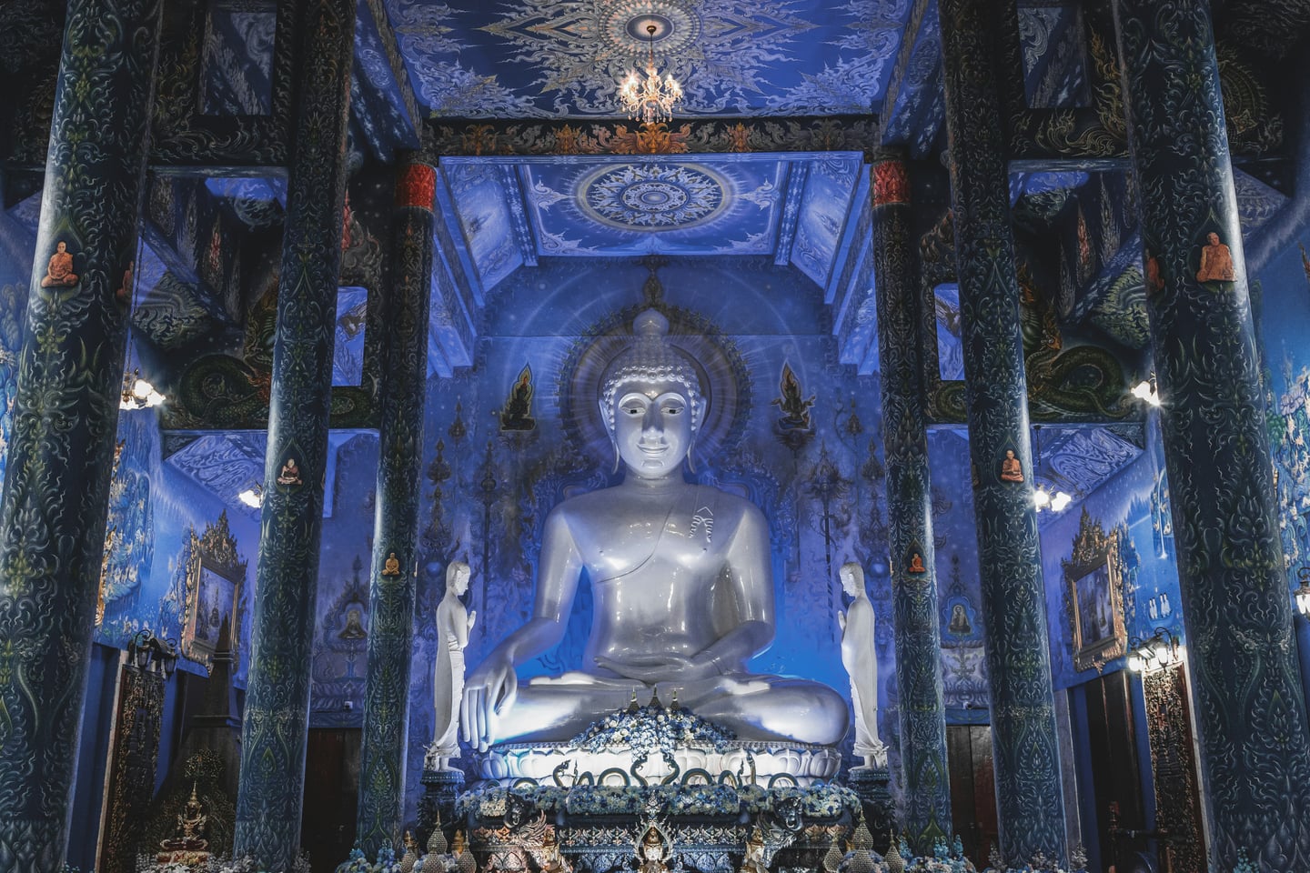 치앙라이 블루 사원, 화려한 푸른색 내부 장식과 중앙에 안치된 거대한 흰색 불상이 조화를 이루며 신비로운 분위기를 연출합니다.