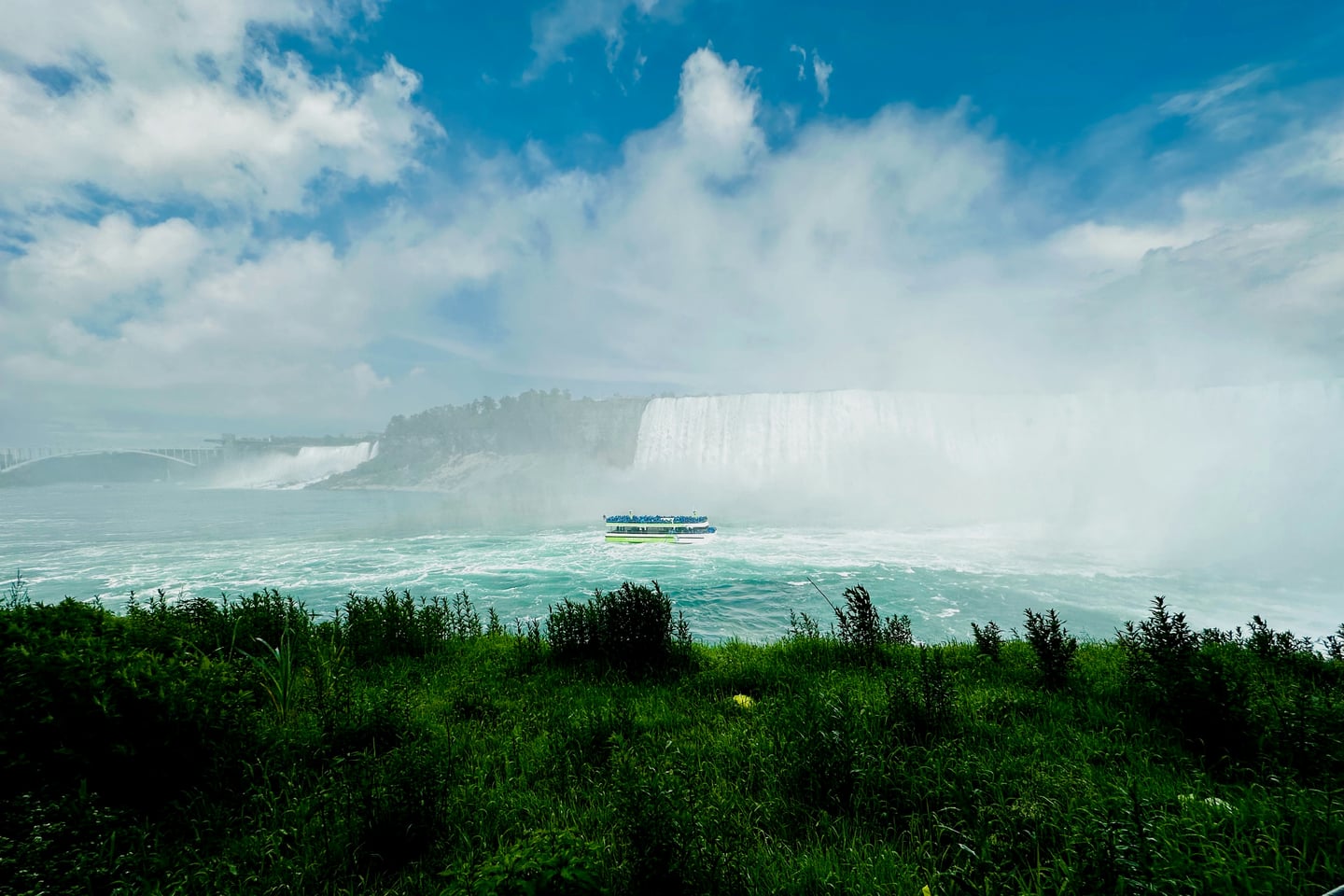 나이아가라 나이아가라 폭포, 거대한 폭포의 물안개 속을 항해하는 유람선과 푸른 풀밭이 어우러진 웅장한 풍경입니다.