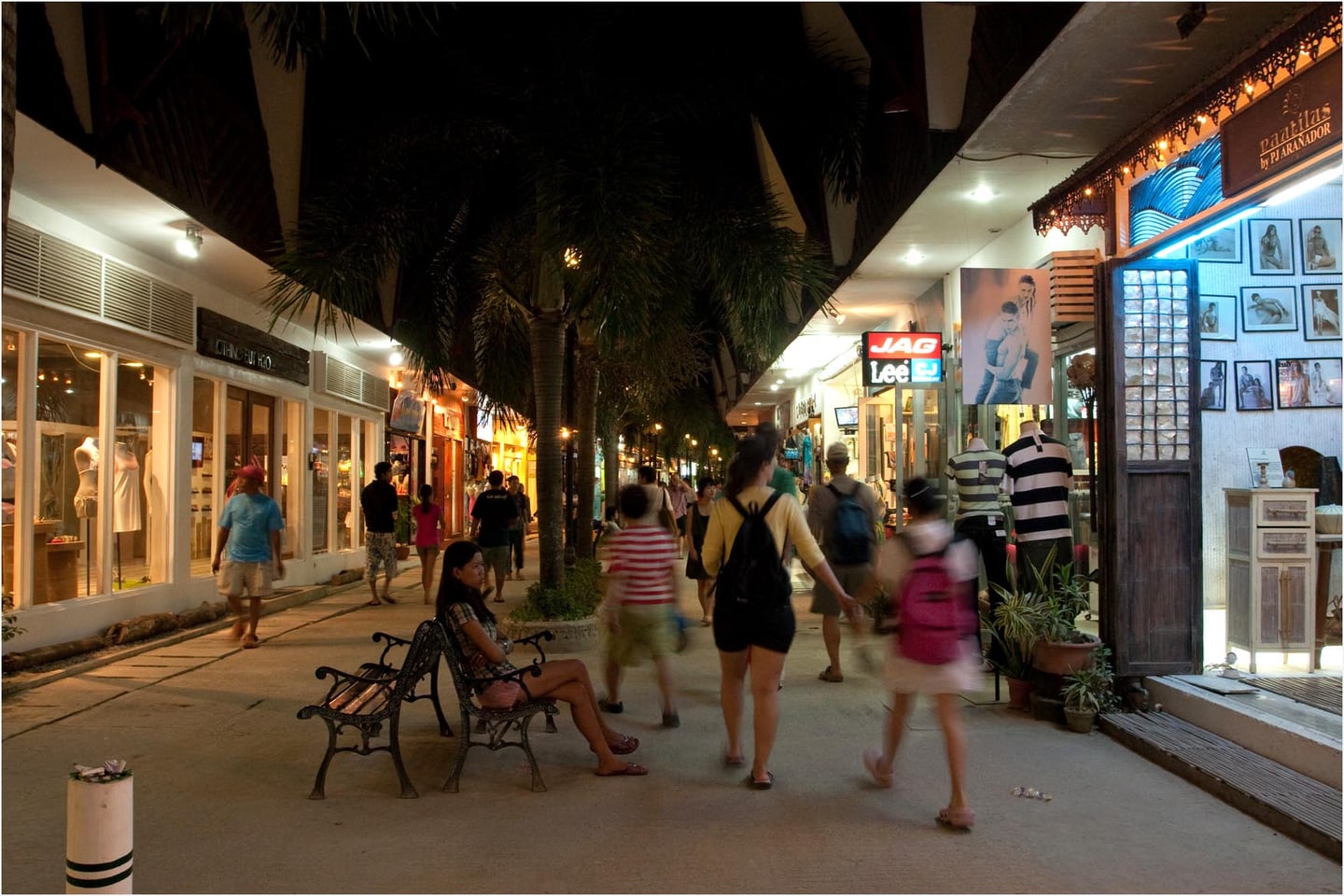 보라카이 디몰, 화려한 조명이 켜진 상점가 사이로 야자수가 늘어선 거리를 산책하는 관광객들의 활기찬 밤 풍경입니다.