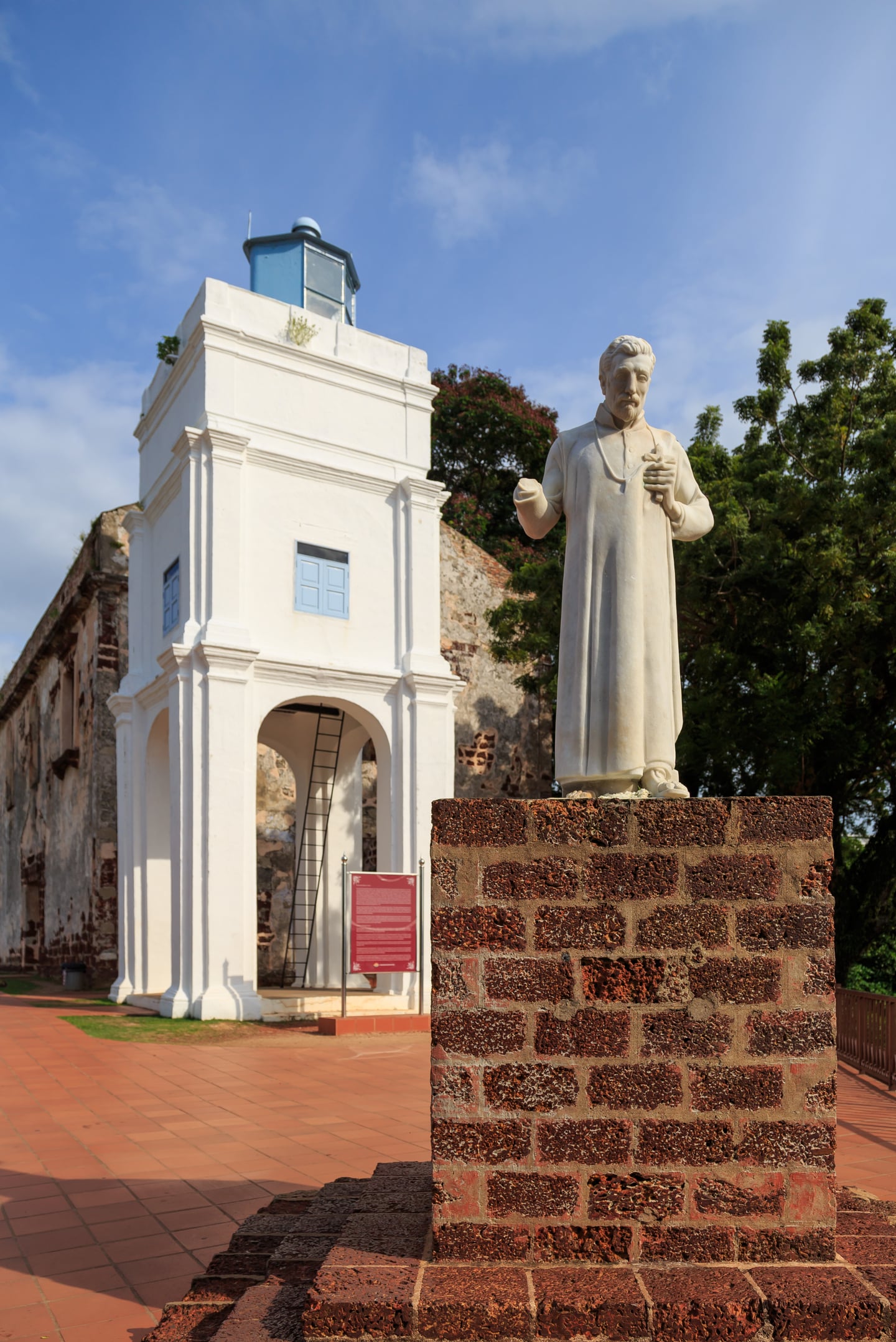 말라카 세인트 폴 성당, 푸른 하늘 아래 하얀 종탑과 성 프란치스코 하비에르 동상이 어우러진 유적지의 평화로운 풍경입니다.
