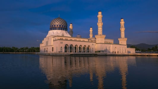 코타키나발루 이슬람사원, 황혼의 푸른 빛을 배경으로 물 위에 반사된 웅장한 블루 모스크의 전경이 신비로운 분위기를 자아냅니다.