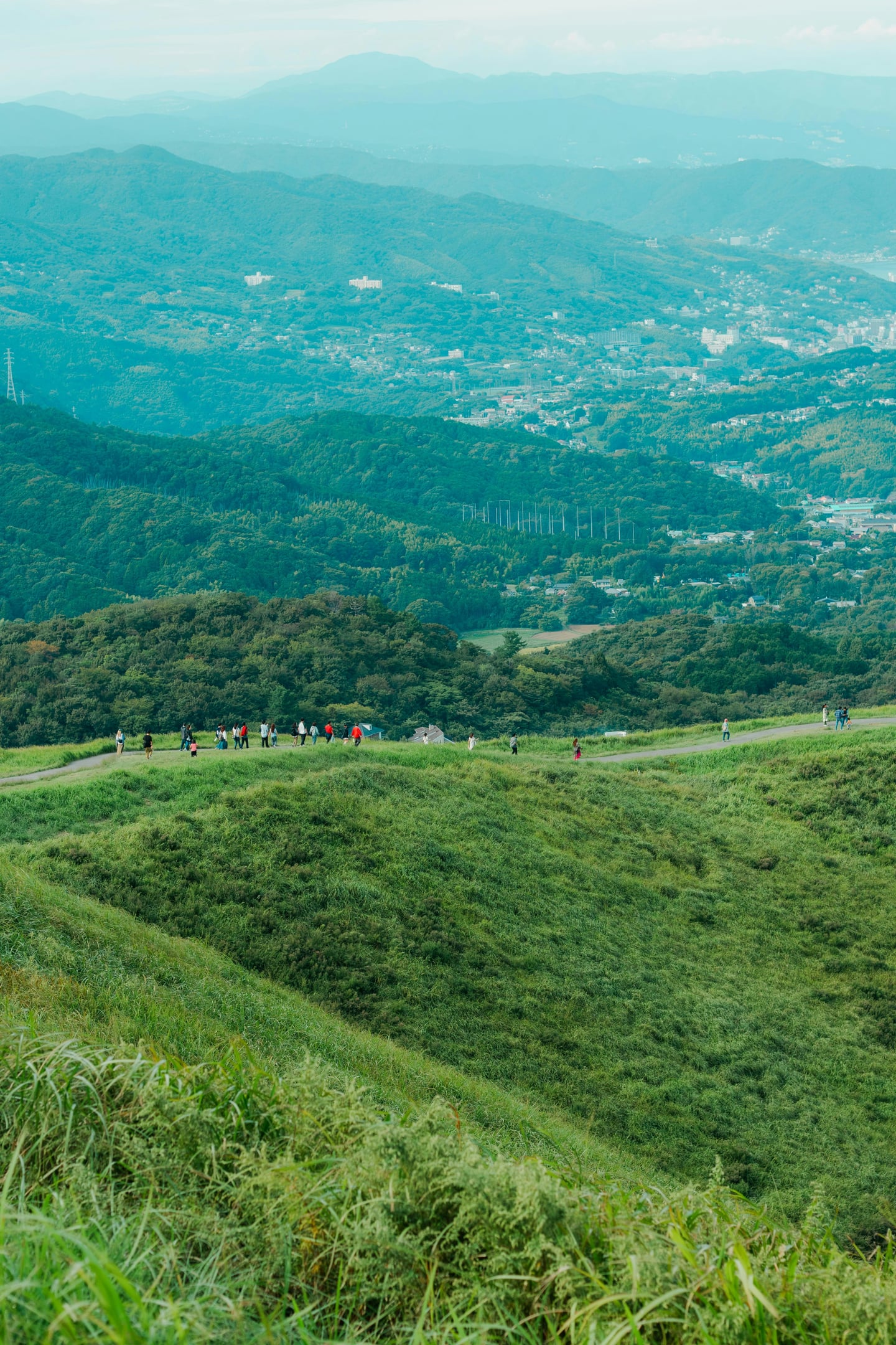 이즈반도 오무로야마, 푸른 능선 산책로를 걷는 사람들과 멀리 펼쳐진 마을 전경이 조화를 이루는 상쾌한 자연 풍경.
