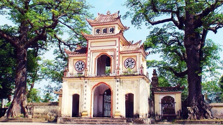 다낭 남선 사찰, 거대한 고목들 사이에 자리 잡은 고풍스러운 노란색 전통 문과 정교한 불교 문양 장식이 돋보이는 풍경입니다.