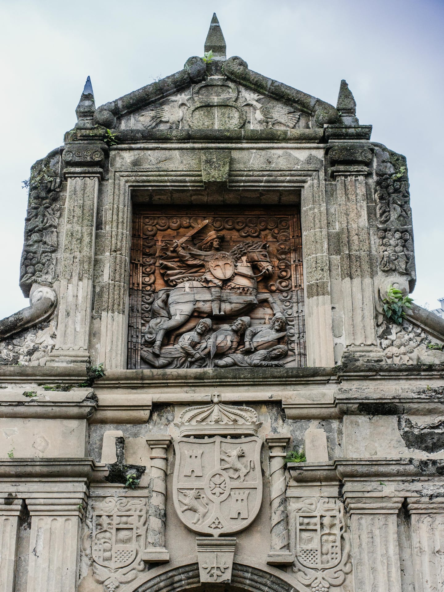 마닐라 산티아고 요새, 고풍스러운 석조 성문 위에 정교하게 조각된 성 야고보의 기마상 부조와 스페인 왕실 문장이 돋보입니다.