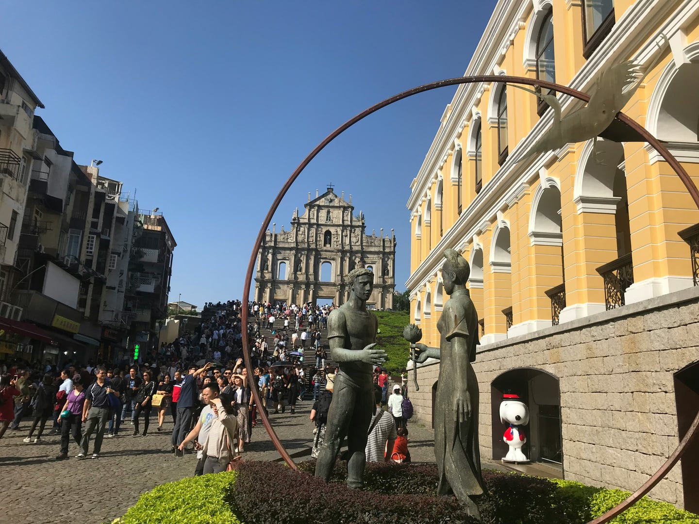 마카오 성 바울 성당 유적, 웅장한 성당 파사드와 전경의 청동 조각상이 어우러진 활기찬 광장의 모습입니다.