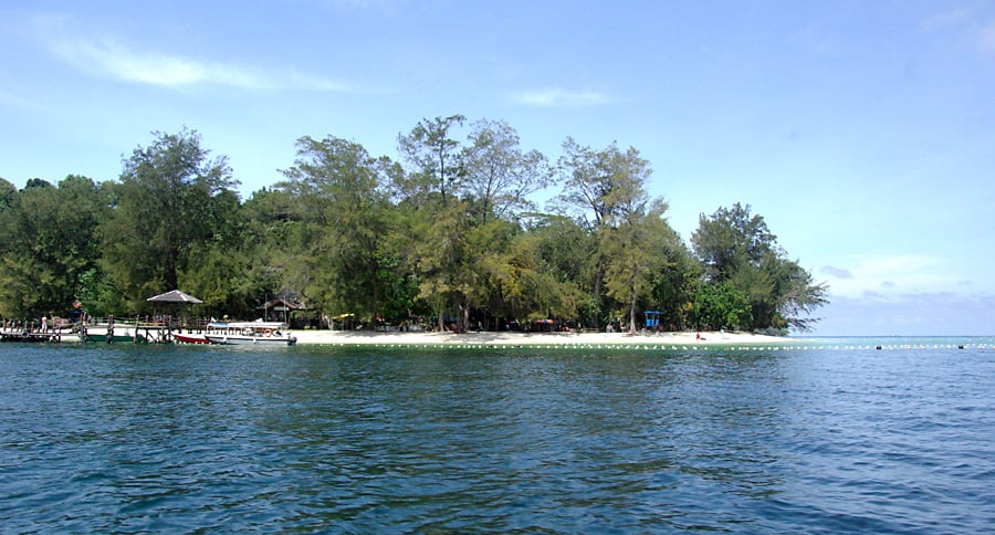 코타키나발루 마무틱 섬, 에메랄드빛 바다와 울창한 숲이 어우러진 해변가에 하얀 보트가 정박해 있는 평화로운 풍경입니다.