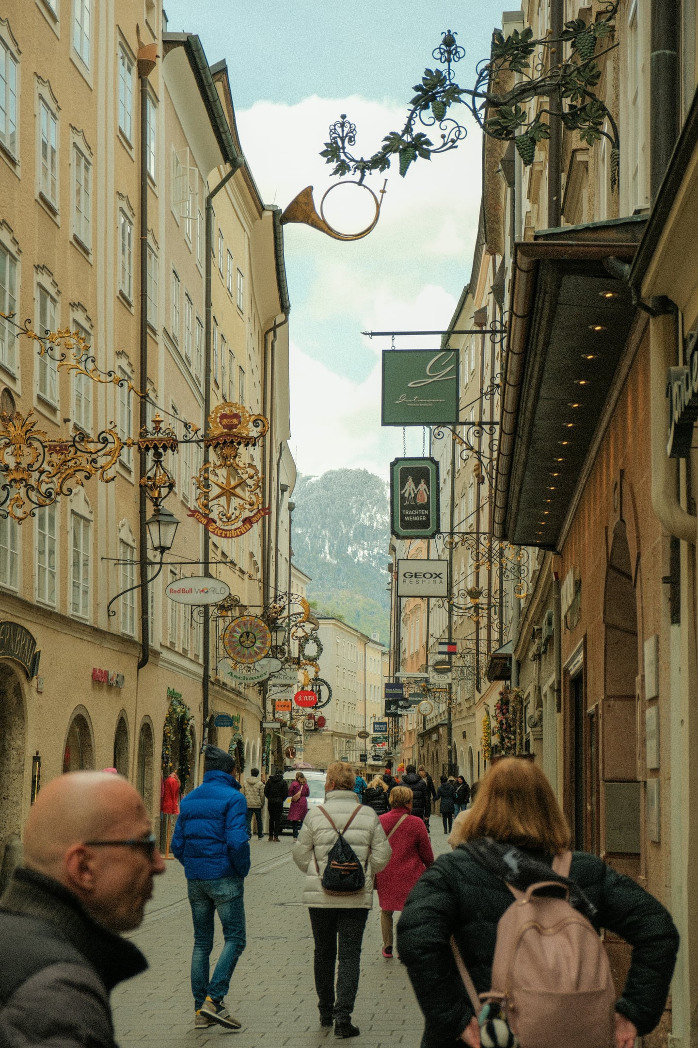 잘츠부르크 게트라이데 거리, 고풍스러운 건물들 사이로 화려한 철제 세공 간판들이 줄지어 늘어선 좁고 활기찬 쇼핑 골목의 풍경입니다.