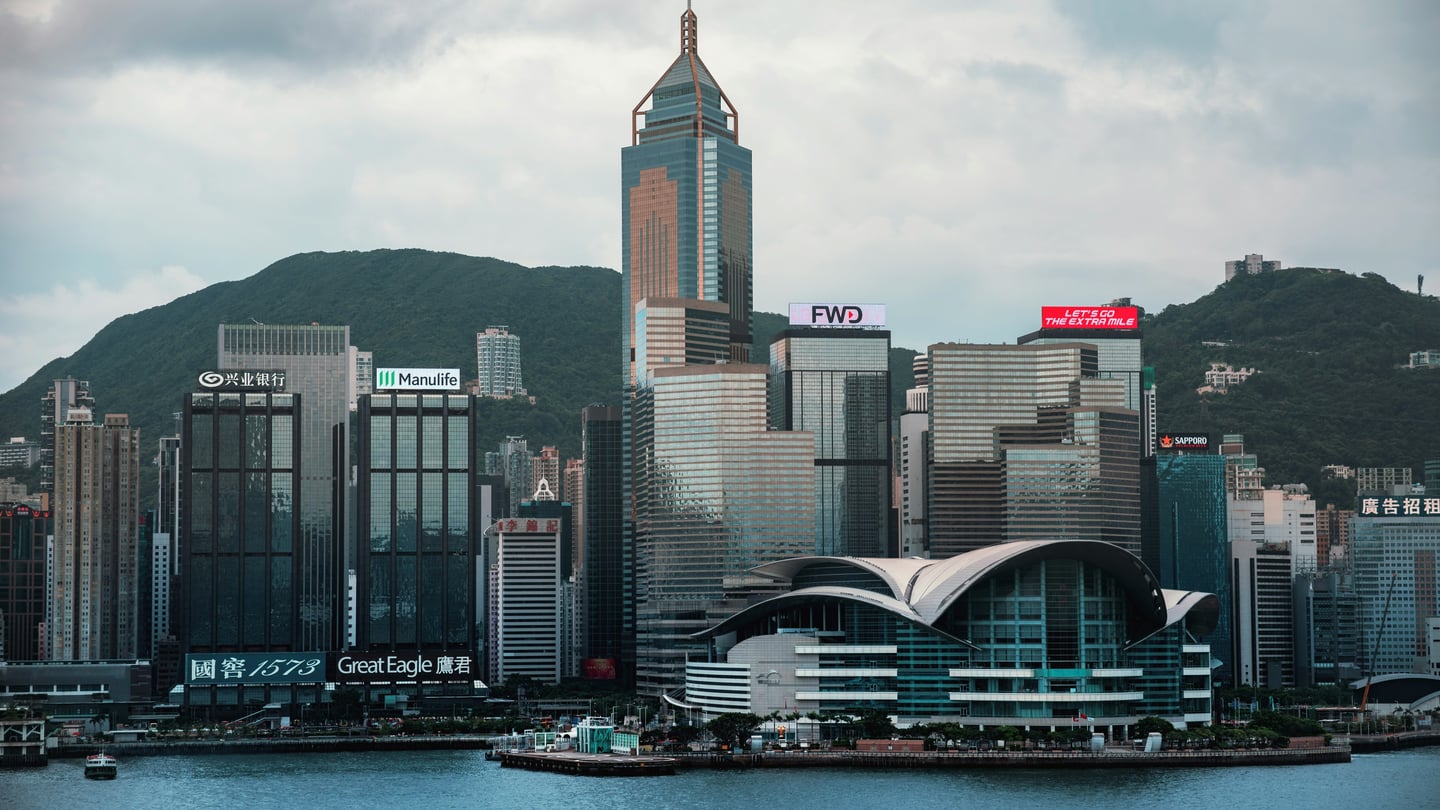 홍콩 침사추이 해변 산책로, 빅토리아 항구 너머로 보이는 웅장한 컨벤션 센터와 화려한 도심 마천루의 전경입니다.