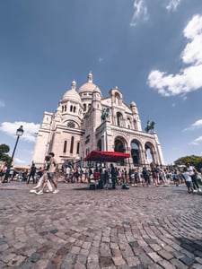 파리 사크레 쾨르 대성당, 푸른 하늘 아래 웅장하게 솟은 하얀 돔과 돌길 광장을 가득 메운 활기찬 관광객들의 모습입니다.