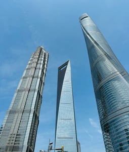 상하이 상하이 세계금융센터, 푸른 하늘 아래 독특한 병따개 모양의 마천루가 진마오 타워 및 상하이 타워와 함께 조화를 이루며 서 있는 풍경입니다.