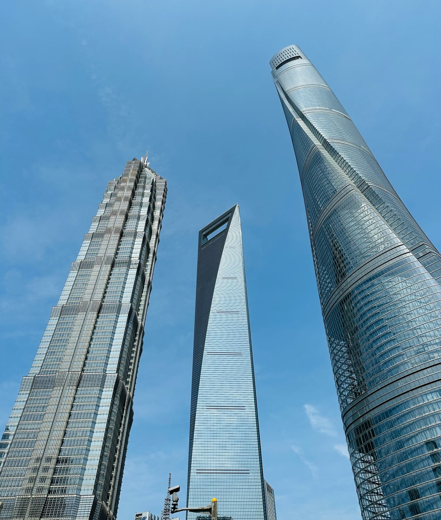 상하이 상하이 세계금융센터, 푸른 하늘 아래 독특한 병따개 모양의 마천루가 진마오 타워 및 상하이 타워와 함께 조화를 이루며 서 있는 풍경입니다.