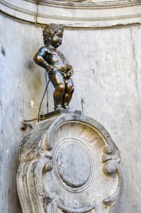 브뤼셀 오줌싸개 동상, 고풍스러운 석조 벽면을 배경으로 서 있는 작은 청동 소년 상의 익살스러운 모습과 물줄기.