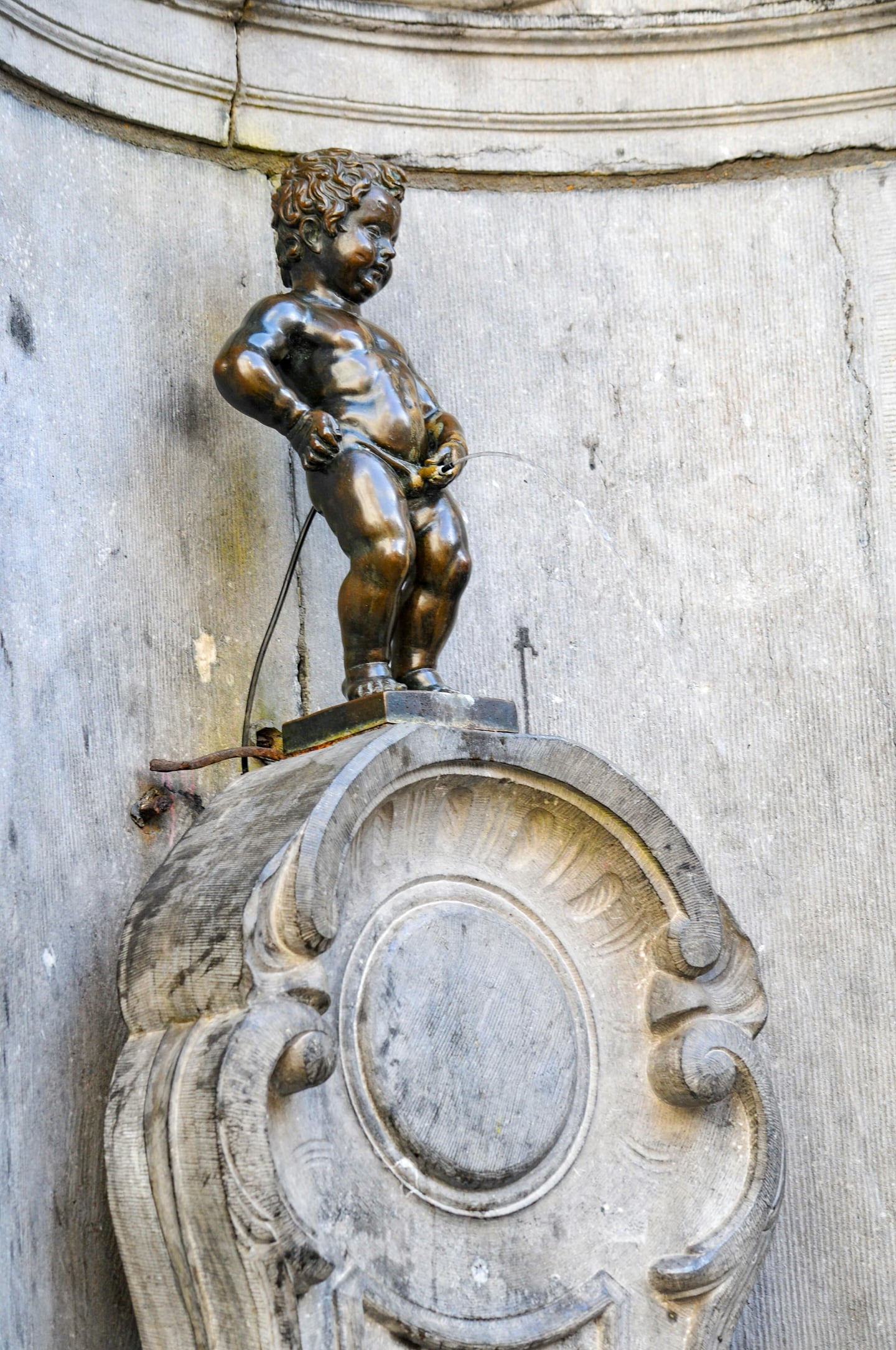 브뤼셀 오줌싸개 동상, 고풍스러운 석조 벽면을 배경으로 서 있는 작은 청동 소년 상의 익살스러운 모습과 물줄기.