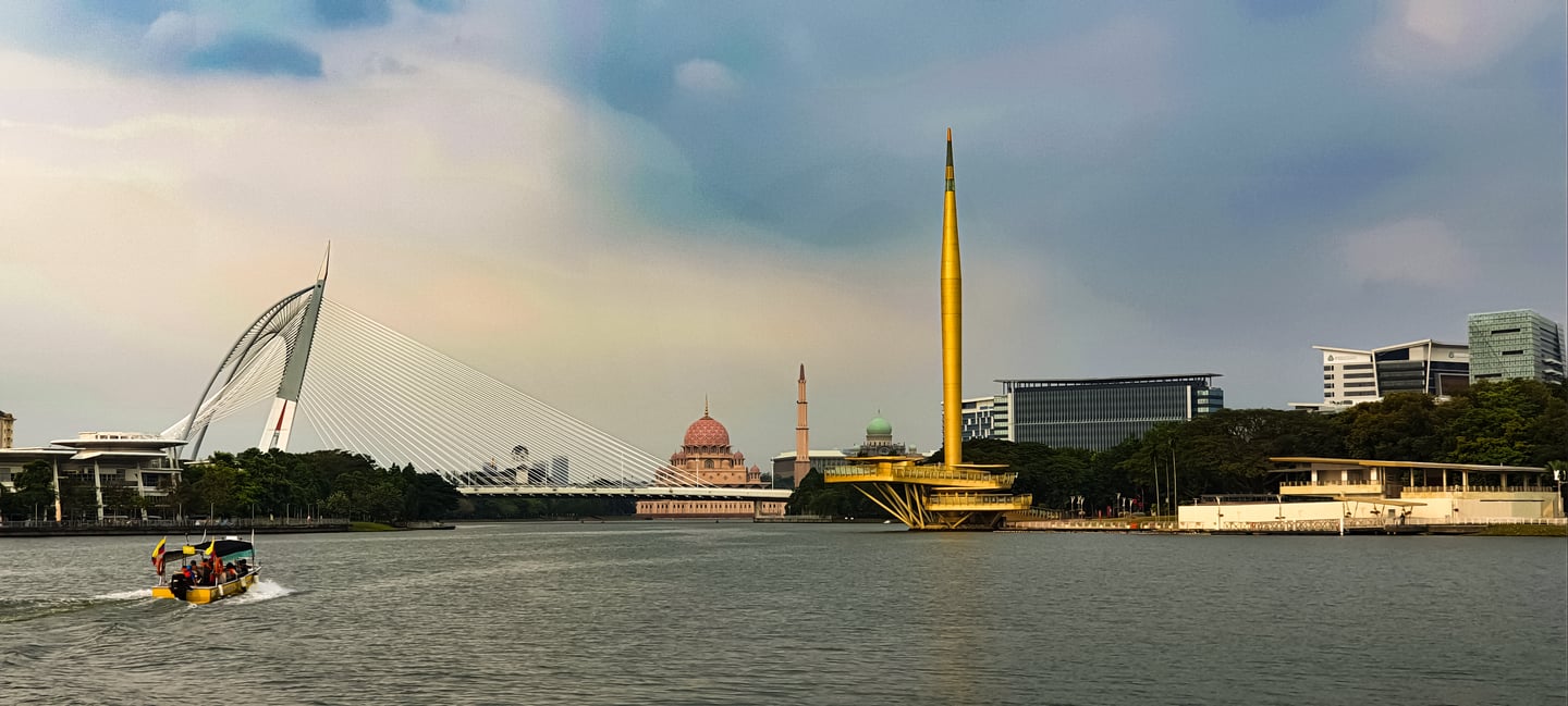 쿠알라룸푸르 푸트라자야, 잔잔한 호수 위로 세리 사우자나 다리와 분홍빛 푸트라 모스크가 어우러진 평화로운 도시의 전경입니다.