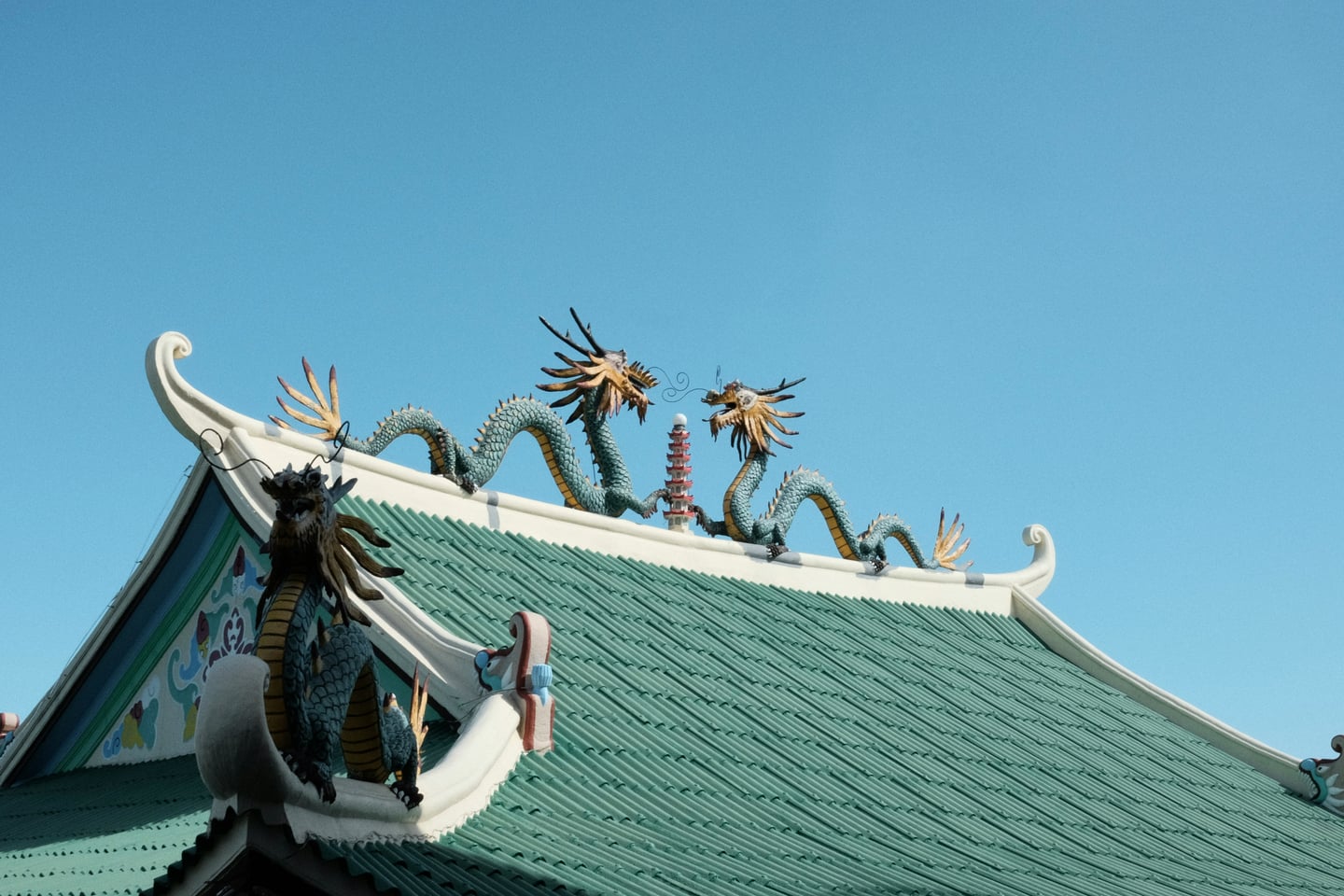 세부 도교 사원, 맑고 푸른 하늘 아래 초록색 기와지붕 위에서 서로 마주 보고 있는 정교한 푸른 용 조각상들의 웅장한 모습.