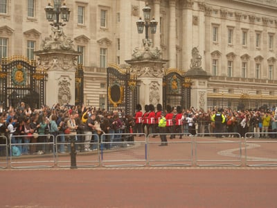 런던 버킹엄 궁전 근위병 교대식, 화려한 금색 장식의 궁전 정문을 배경으로 붉은 제복의 근위병들이 행진하며 관광객들의 시선을 사로잡는 모습입니다.