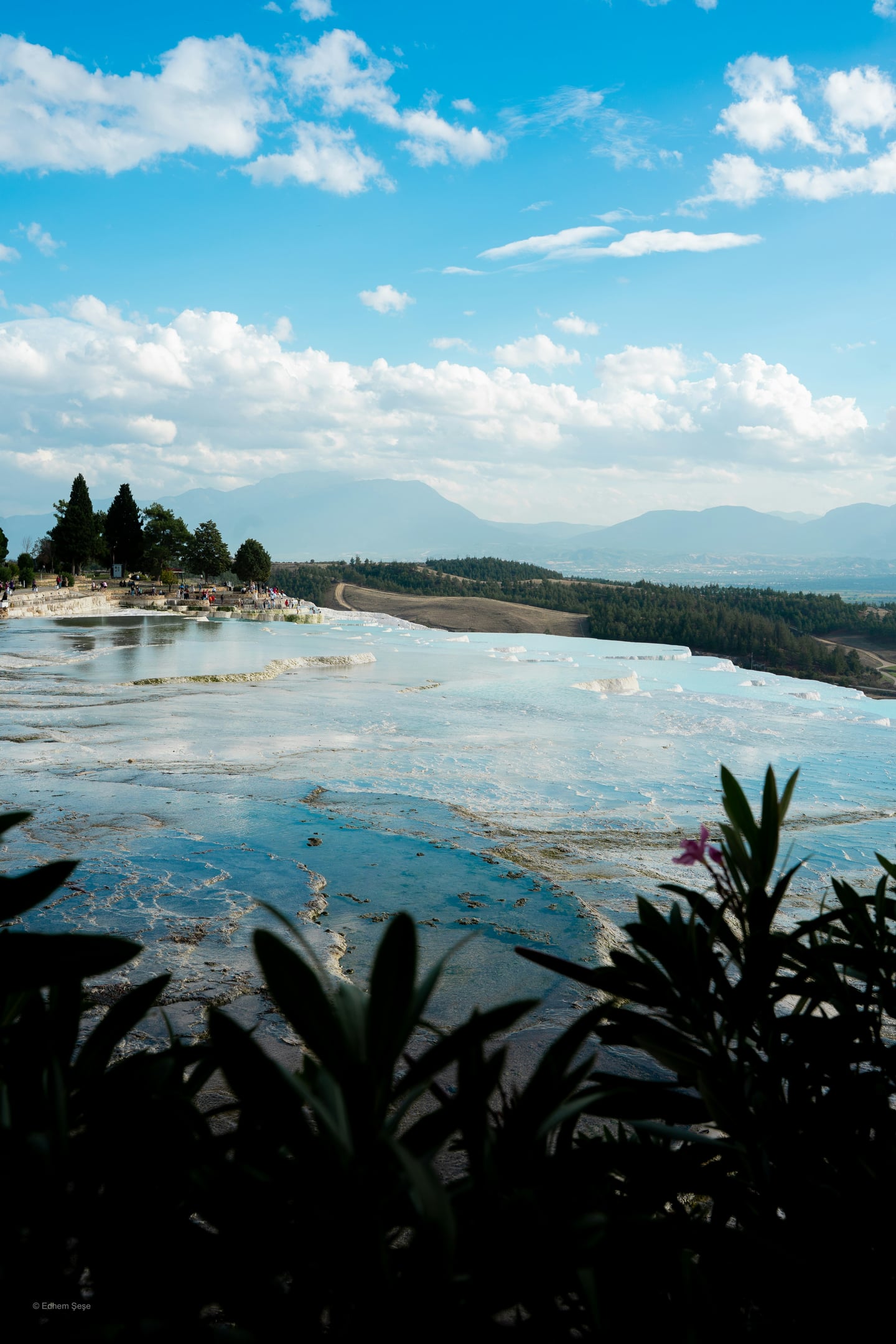 파묵칼레 노천온천, 눈부시게 하얀 석회 테라스 위로 에메랄드빛 온천수가 층층이 고여 있고 푸른 하늘과 산맥이 펼쳐진 이국적인 풍경입니다.