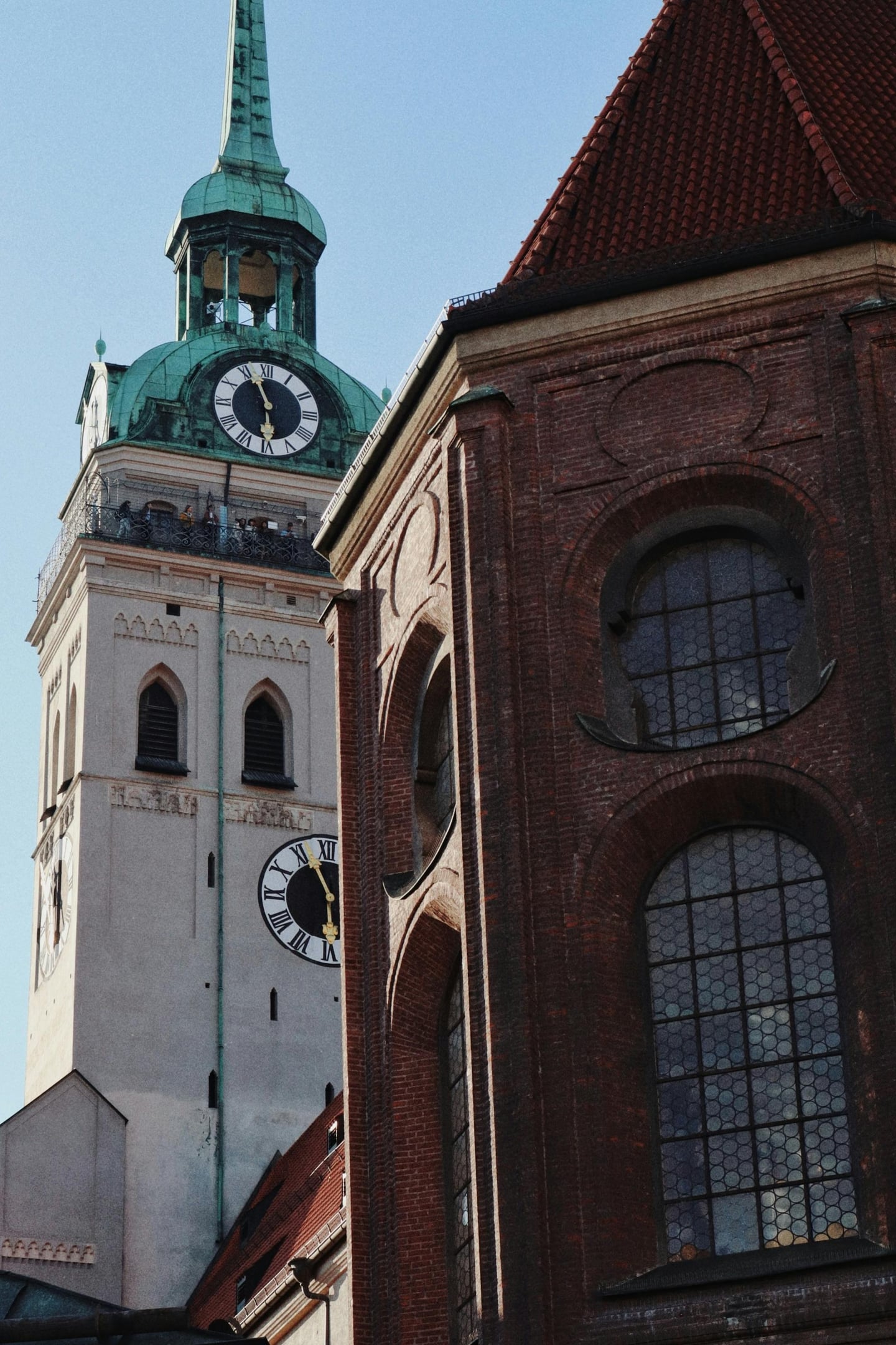 뮌헨 성 피터 교회, 푸른 하늘 아래 우뚝 솟은 고풍스러운 시계탑과 붉은 벽돌 건물의 조화로운 풍경입니다.