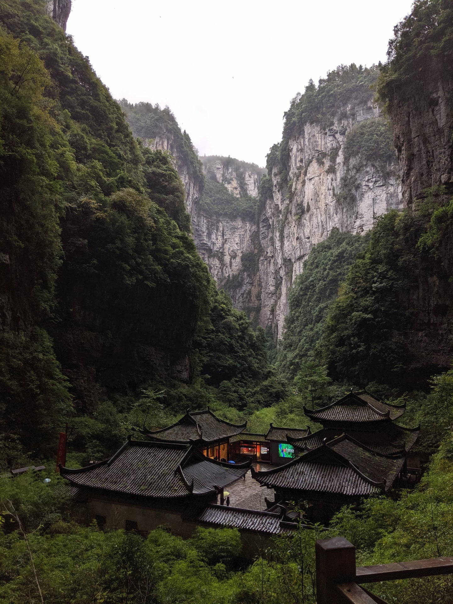 충칭 우롱 카르스트, 거대한 석회암 절벽 아래 자리 잡은 고풍스러운 천복관역의 기와지붕과 울창한 협곡의 신비로운 풍경입니다.