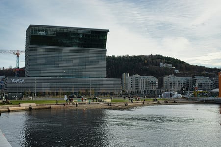 오슬로 뭉크 미술관, 바다를 마주하며 상단이 비스듬하게 기울어진 독특한 회색빛 현대식 타워 건물이 수변 광장과 어우러진 풍경입니다.