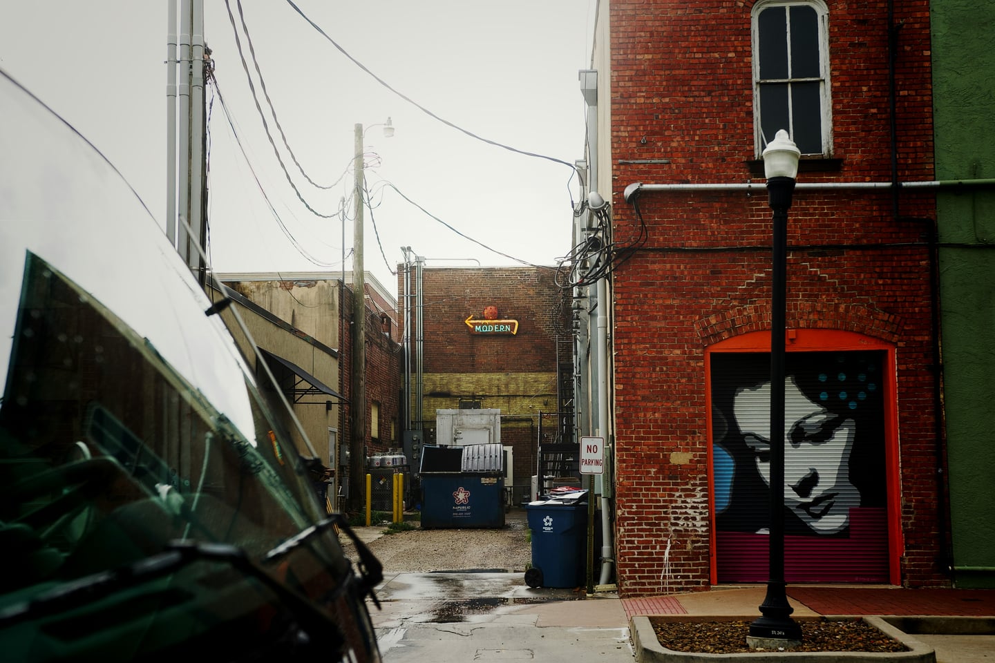 범용 골목 벽화 여성, 붉은 벽돌 건물 사이 좁은 골목길 셔터에 그려진 감각적인 여성 얼굴 벽화와 빈티지한 네온사인 풍경입니다.