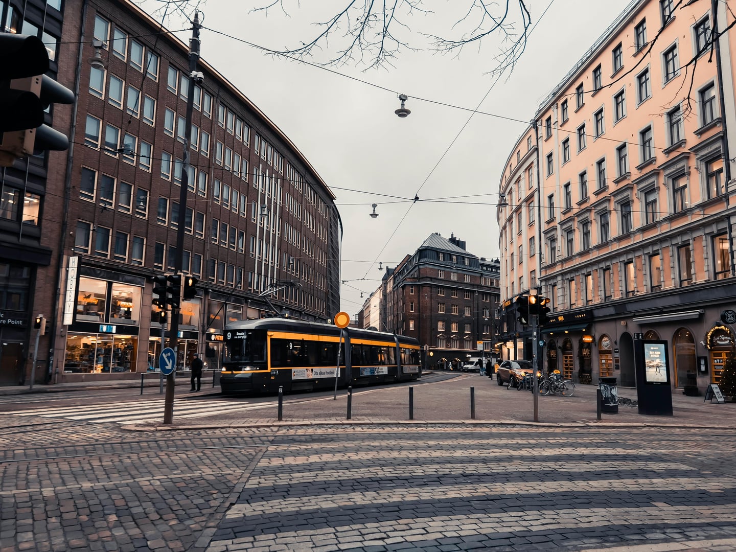헬싱키 만네르헤임 거리, 고전적인 건물들 사이로 노란색 포인트가 들어간 현대적인 트램이 돌길 교차로를 가로지르는 평화로운 도심 풍경입니다.