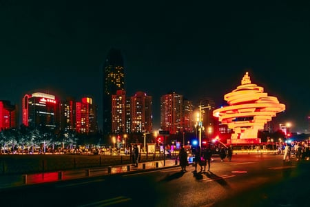 칭다오 5.4 광장 레이저쇼, 밤하늘 아래 붉게 빛나는 오월의 바람 조형물과 화려한 도심 빌딩 숲이 어우러진 환상적인 야경 명소의 풍경입니다.