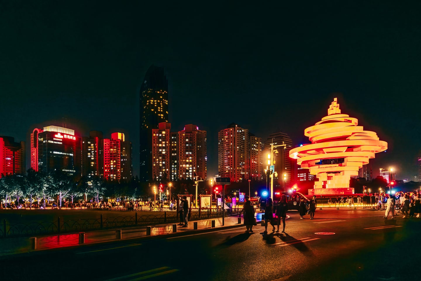 칭다오 5.4 광장 레이저쇼, 밤하늘 아래 붉게 빛나는 오월의 바람 조형물과 화려한 도심 빌딩 숲이 어우러진 환상적인 야경 명소의 풍경입니다.