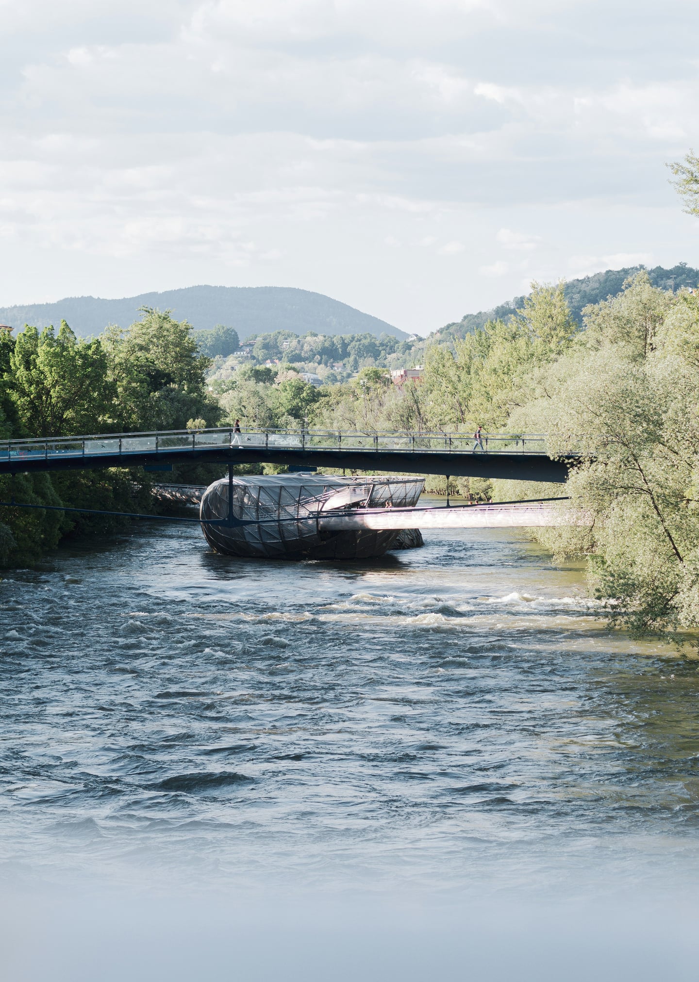 그라츠 무어인젤, 무어강의 푸른 물결 위에 떠 있는 독특한 조개 모양의 금속 구조물과 이를 연결하는 보행교의 현대적인 조화.