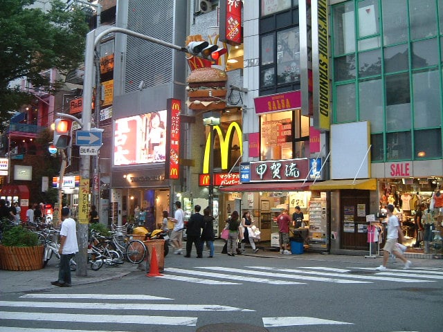 오사카 아메리카무라, 대형 햄버거 간판과 코가류 타코야키 매장이 위치한 번화가에서 시민들이 횡단보도를 건너는 활기찬 일상 풍경입니다.