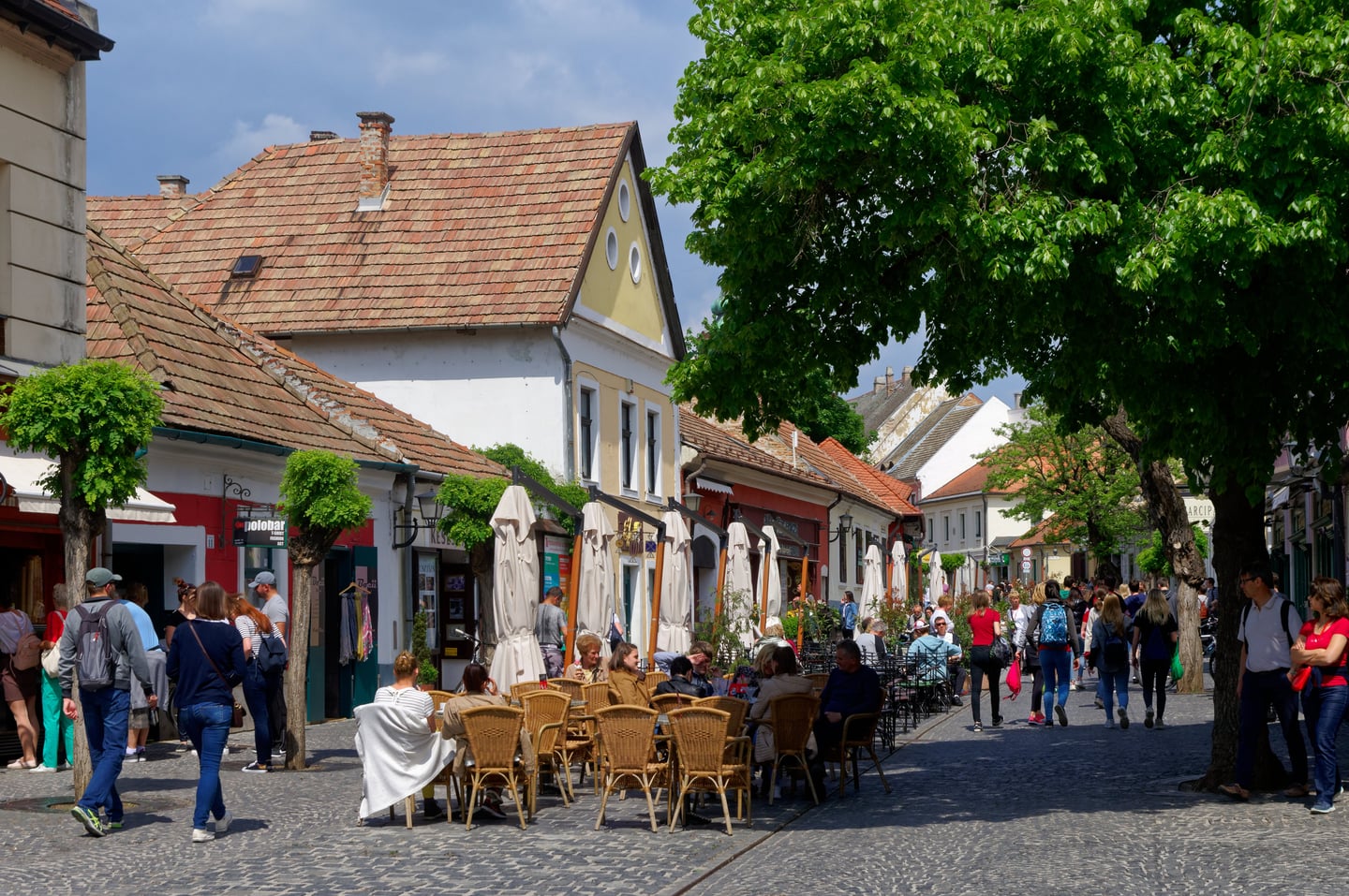 센텐드레 센텐드레, 붉은 기와지붕의 고풍스러운 건물들과 야외 테라스 카페에서 여유를 즐기는 사람들의 활기찬 거리 풍경입니다.