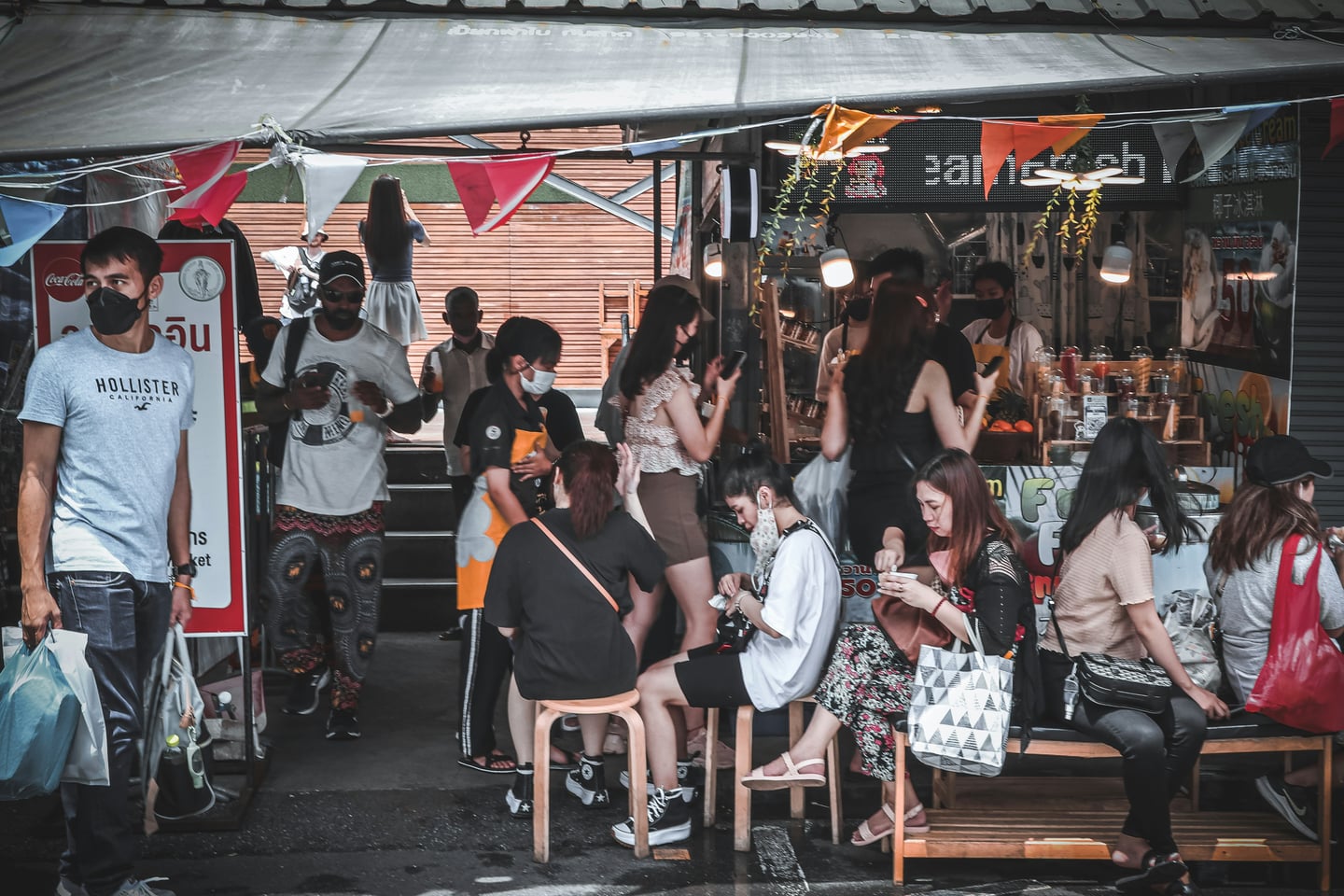 방콕 짜뚜짝 주말시장, 활기찬 시장 골목 노점에서 간식을 즐기며 휴식을 취하는 관광객들의 모습입니다.