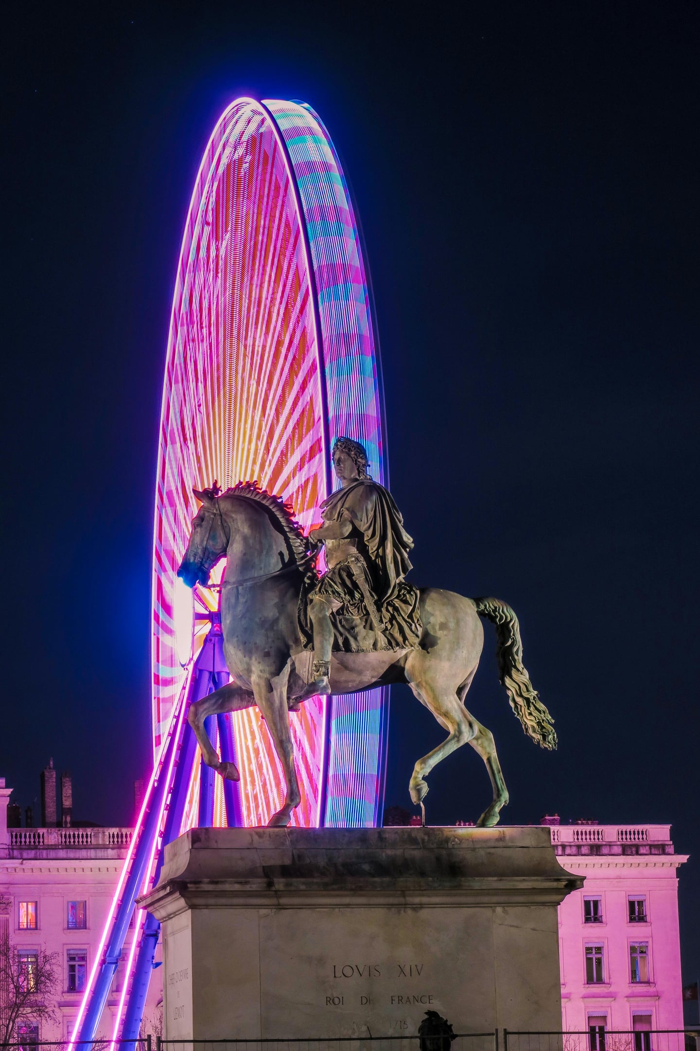 리옹 벨쿠르 광장, 화려한 네온 조명의 대관람차를 배경으로 위엄 있게 서 있는 루이 14세 기마상의 환상적인 야경입니다.